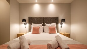 A neatly made bed with two pillows, two bedside lamps, and two rolled towels on the bed.