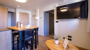 A modern kitchen with wooden countertops, a kettle, and a coffee maker. There is a TV mounted on the wall and a plant on a table.