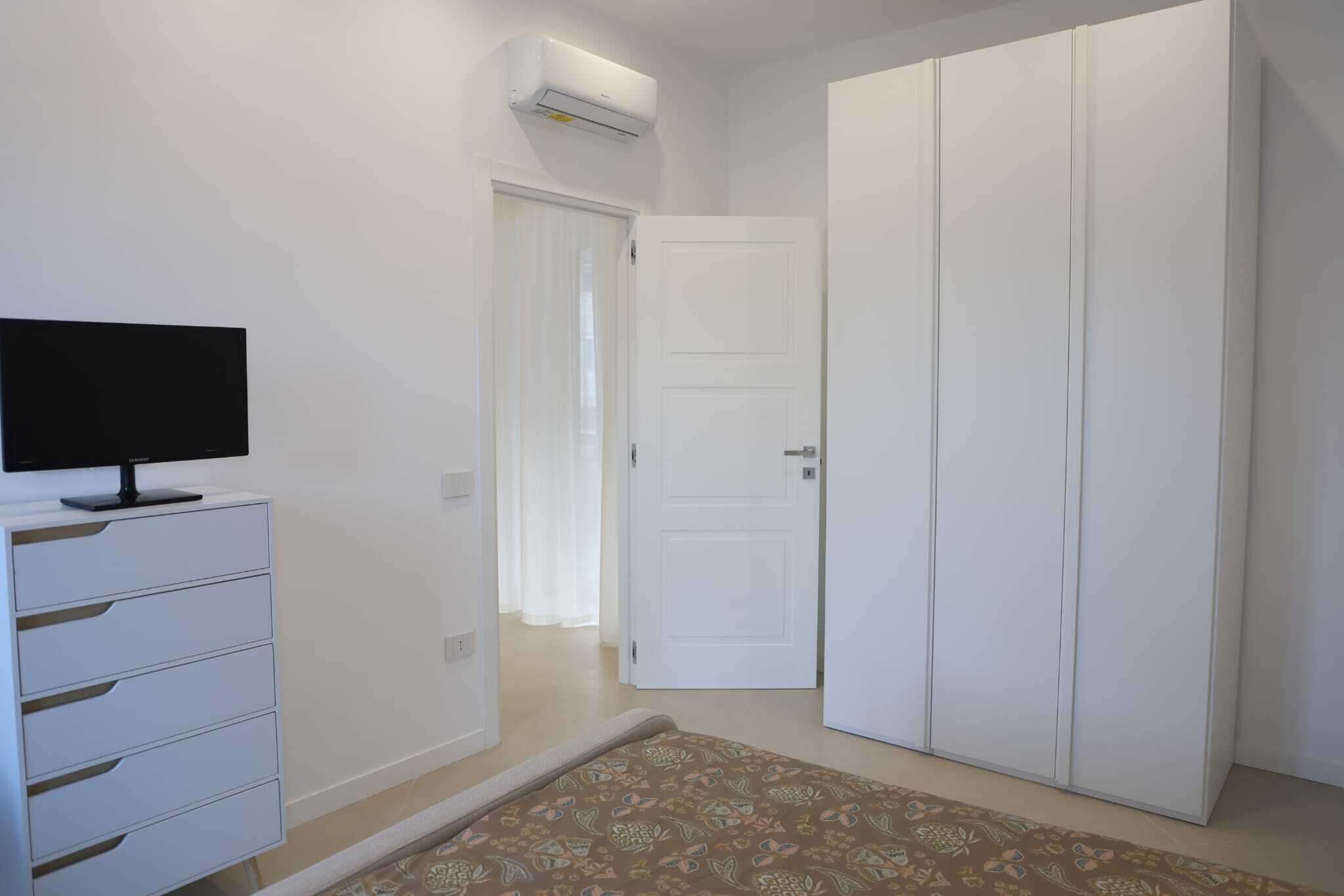 A room with a white wardrobe, a television on a white cabinet, and a patterned rug.