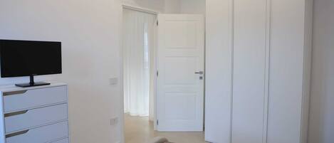 A room with a white wardrobe, a television on a white cabinet, and a patterned rug.