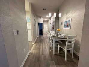 A hallway leading to a dining area with a table set for four, white chairs, and a painting on the wall. - Ground floor condo in Bahama Bay (Davenport)
