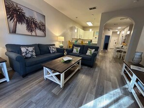 A living room with a sofa, coffee table, and a painting of palm trees. - Ground floor condo in Bahama Bay (Davenport)