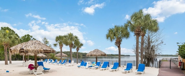 A beach with lounge chairs and thatched umbrellas, a clear sky, and a calm body of water. - Ground floor condo in Bahama Bay (Davenport)