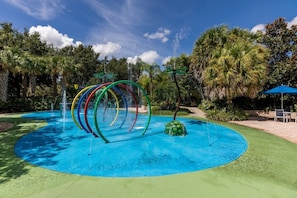 A water play area with multiple water jets and a circular pool, surrounded by palm trees and greenery. - Updated Bahama Bay Condo | 2BR/2BA | Patio (Davenport)