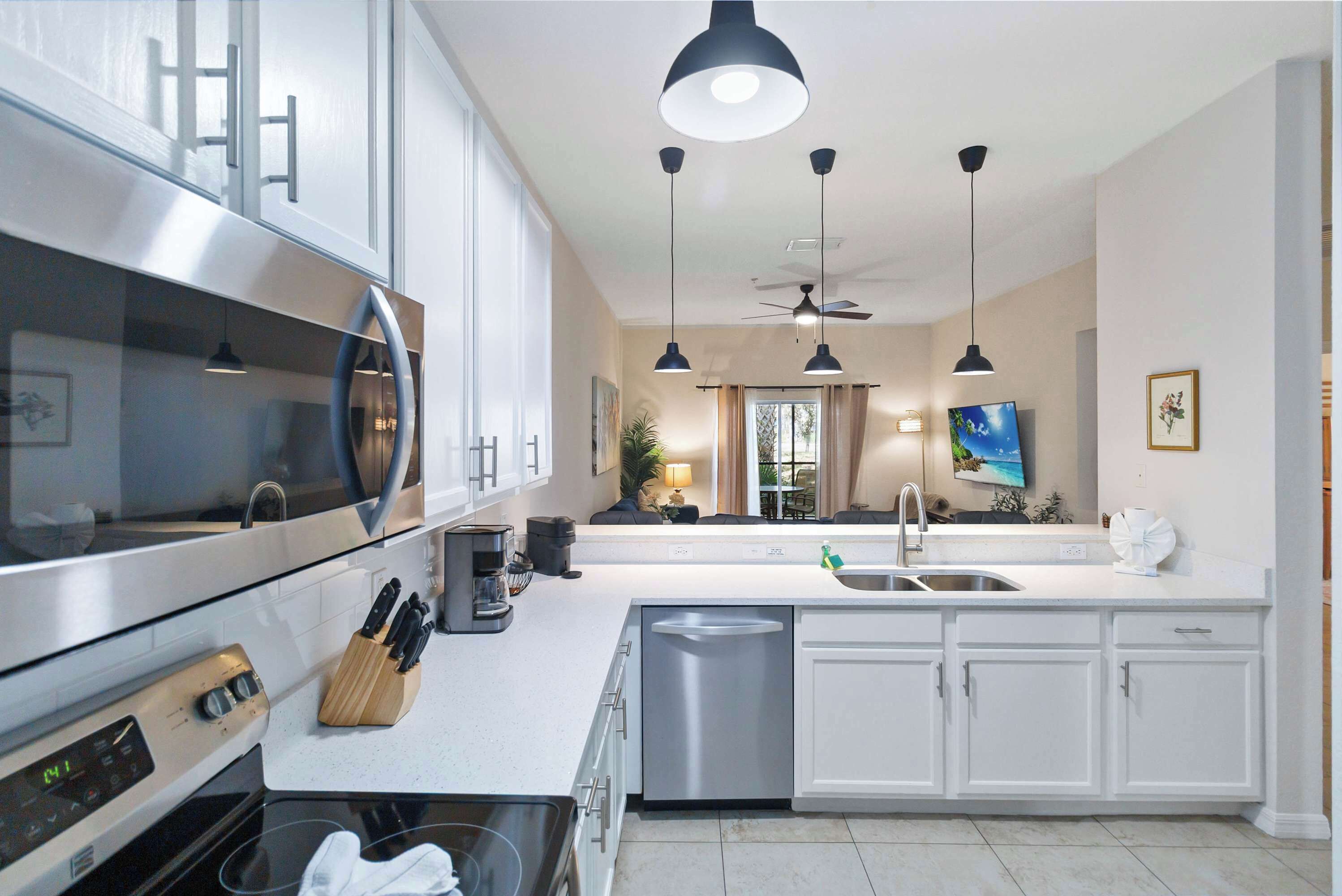 Una cocina moderna con electrodomésticos de acero inoxidable, armarios blancos e iluminación colgante.