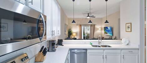 Una cocina moderna con electrodomésticos de acero inoxidable, armarios blancos e iluminación colgante.