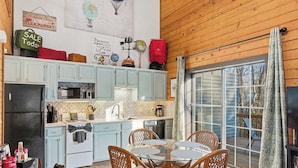A compact kitchen with light blue cabinets, a dining area with wicker chairs, and a large sliding glass door leading to an outdoor deck. - The Travelers Nest For 8 (Branson)