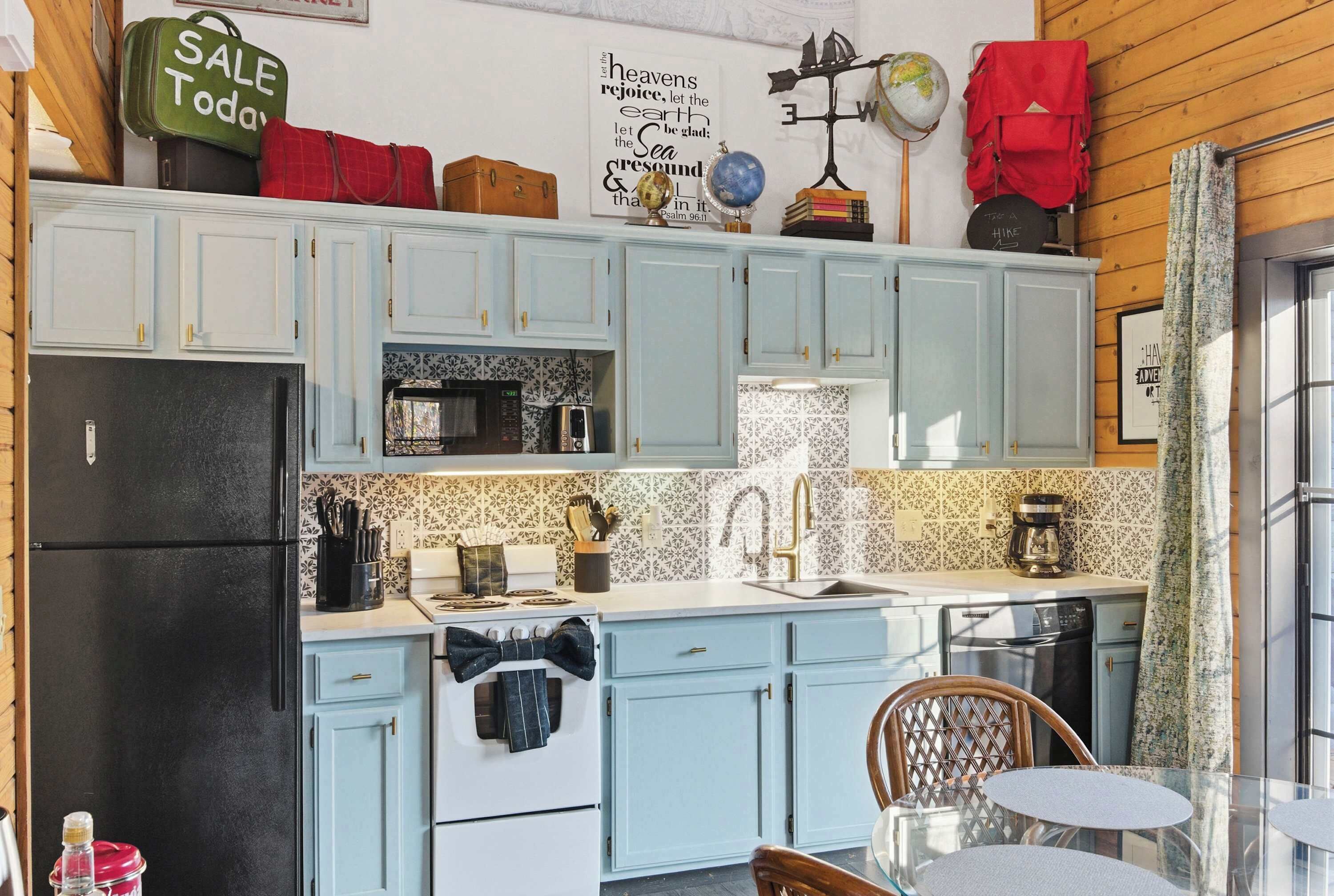 A compact kitchen with light blue cabinets, a black refrigerator, and a small dining area with a table and chairs.