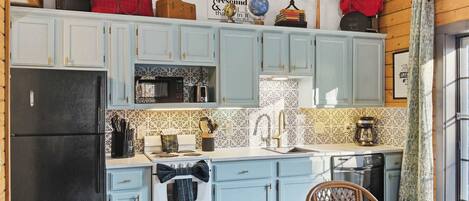 A compact kitchen with light blue cabinets, a black refrigerator, and a small dining area with a table and chairs.