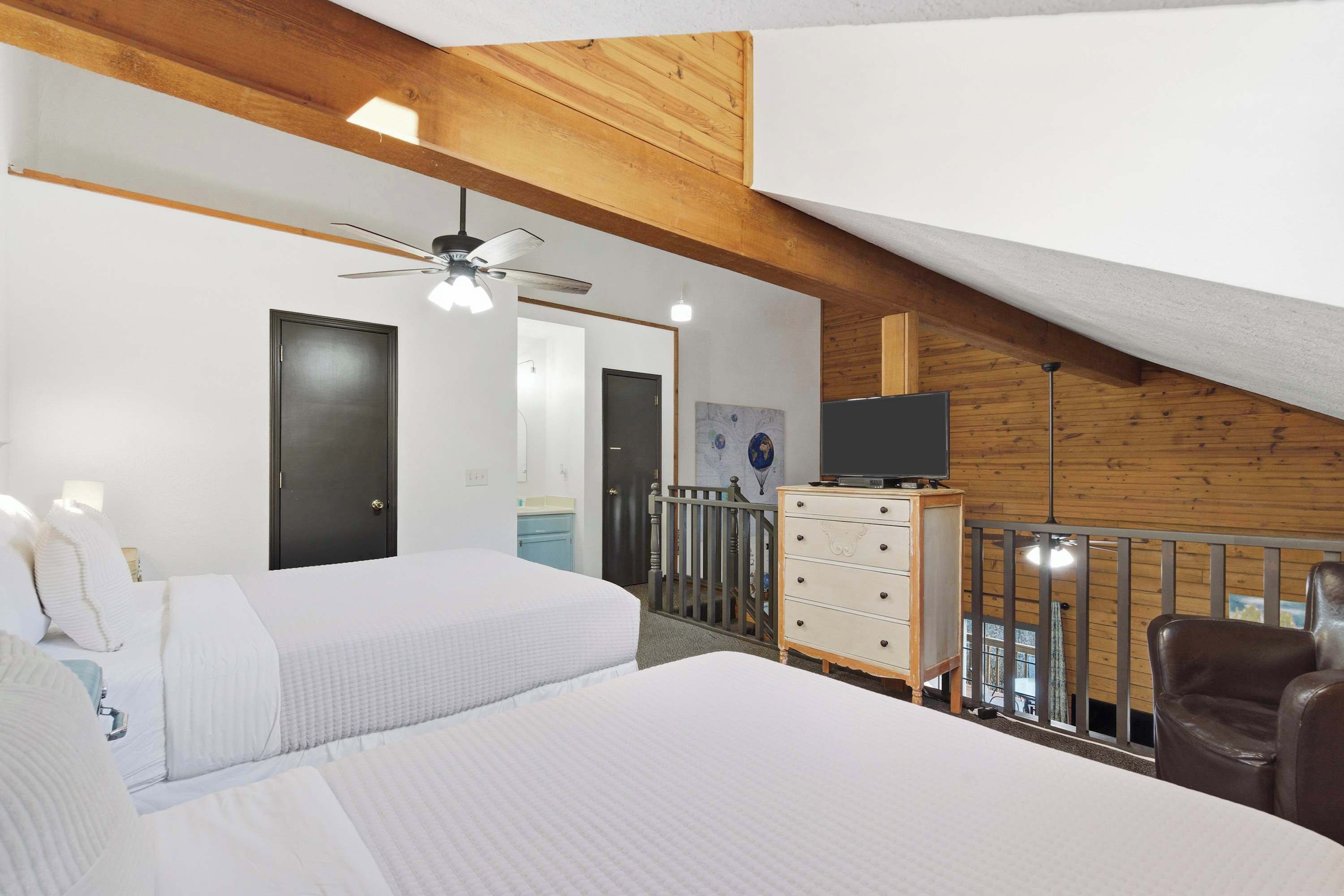 A bedroom with two beds, a dresser, a television, and a balcony with a railing.