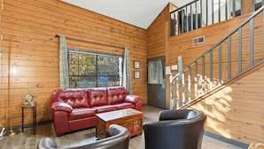 A cozy wooden cabin interior with a red leather sofa, a wooden coffee table, and a staircase leading to an upper level. - The Travelers Nest For 8 (Branson)