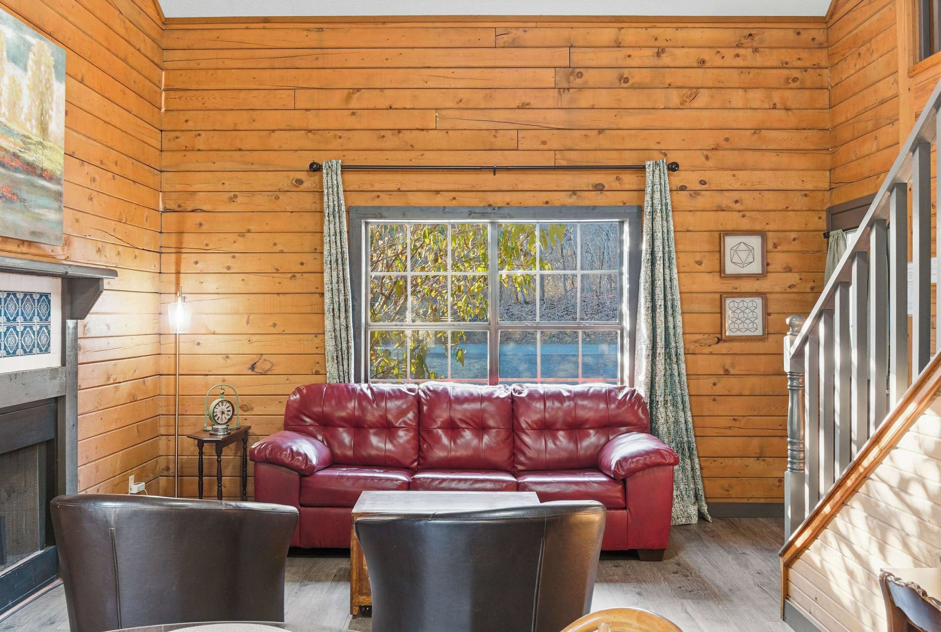 Une pièce chaleureuse avec des murs en bois, un canapé en cuir rouge, une petite table et une fenêtre avec des rideaux.