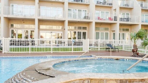 Un hotel con piscina, varios balcones y un área exterior cercada.