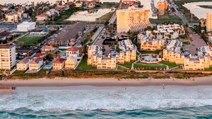 Vista aérea de un complejo turístico costero con propiedades frente al mar, un área de piscina central y una playa.