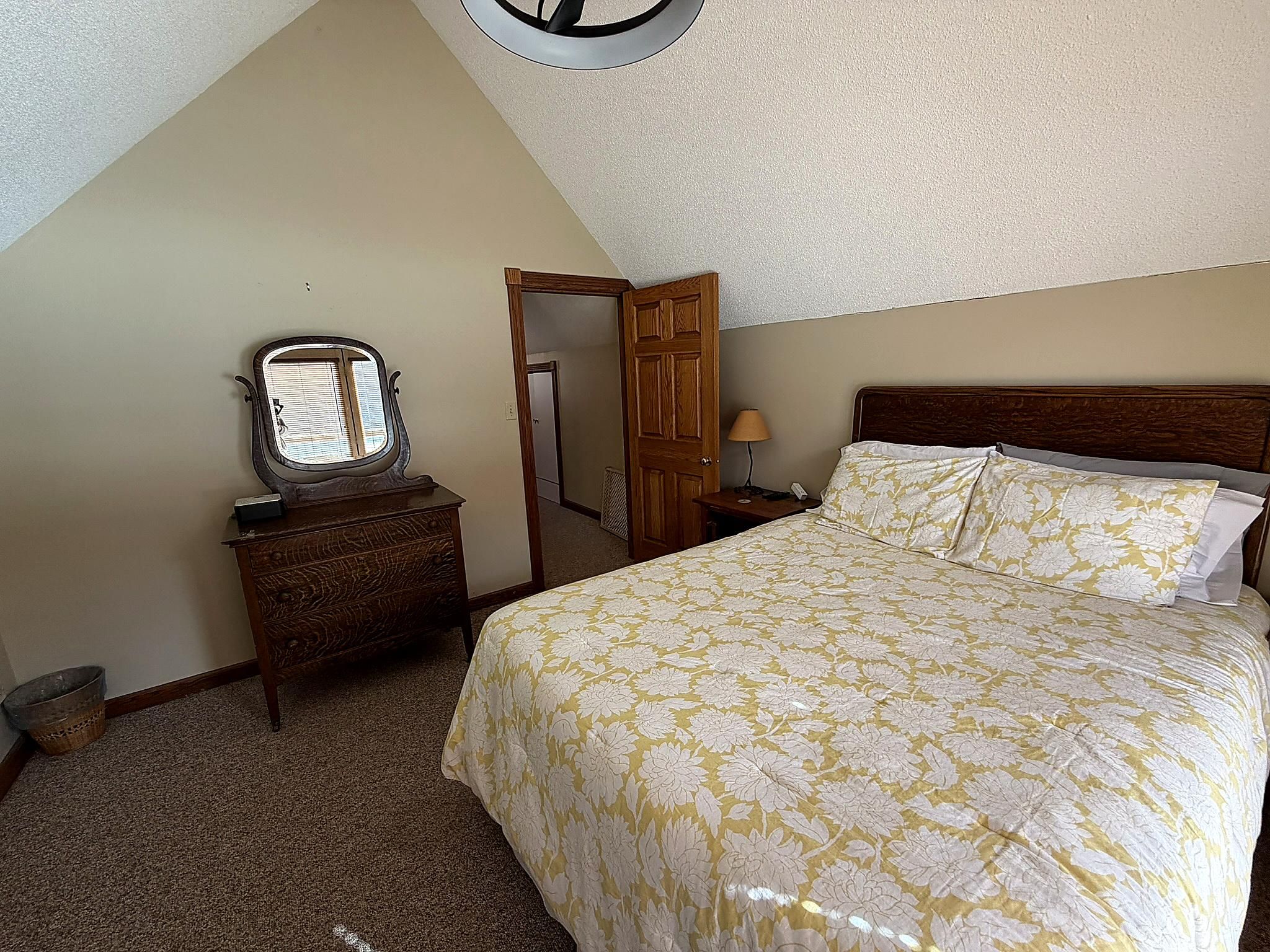 A bedroom with a bed, a dresser, a mirror, a door, and a lamp.
