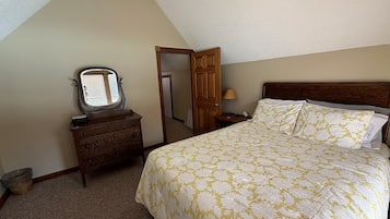 A bedroom with a bed, a dresser, a mirror, a door, and a lamp.