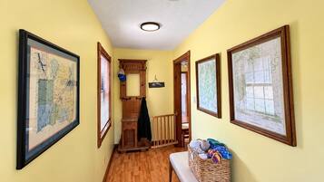 A hallway with wooden flooring, a bench with a basket, and framed maps on the walls.