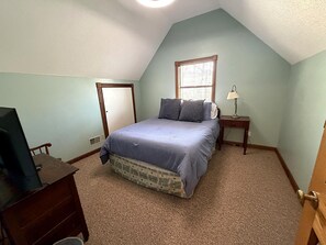 A bedroom with a bed, a nightstand, a lamp, a television, and a door. - Medora Getaway, Charming Lakefront Retreat in Scenic Medora, Indiana (Medora)
