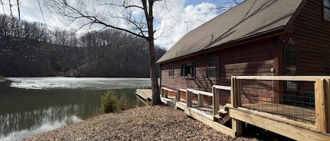 A wooden cabin with a dock extending into a lake, surrounded by trees and a forested area.