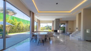 Un'ampia area interna con pavimento in marmo, un tavolo rotondo e una grande finestra vista piscina e vegetazione.