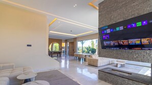 Un soggiorno moderno con una grande televisione a schermo piatto che mostra servizi di streaming, una zona salotto accogliente con divano e tavolino, e un'area pranzo con tavolo e sedie.