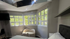 A bedroom with a large bed, a sofa, and a window with a view of greenery. - Hotel Casa Recoleta (Buenos Aires)