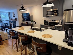 A modern kitchen with a large island, bar stools, stainless steel appliances, and a flat-screen TV.