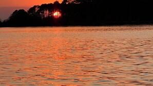 Un atardecer sobre una superficie de agua tranquila, con la silueta de árboles al fondo.