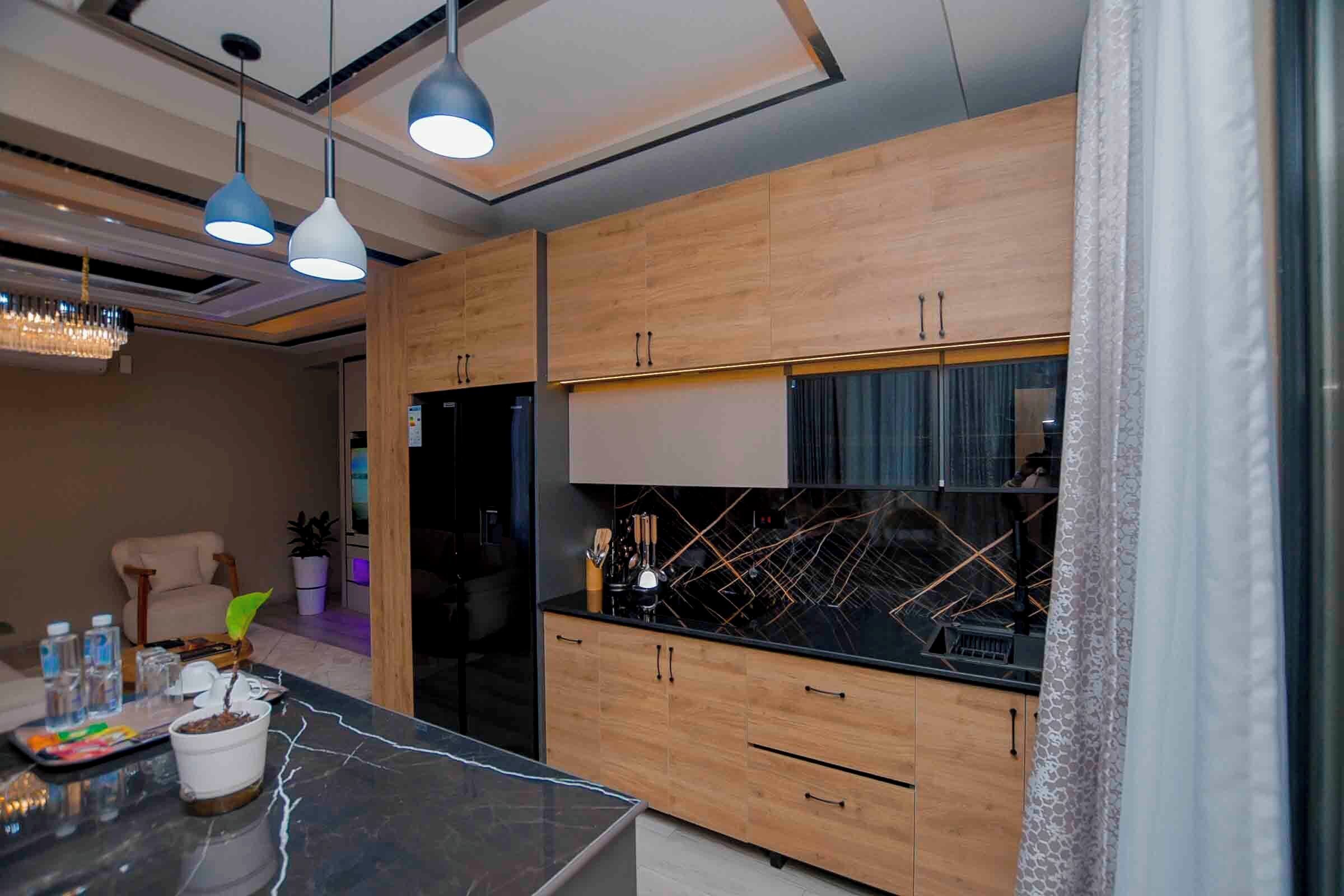 A modern kitchen with wooden cabinets, a black countertop, and pendant lighting.