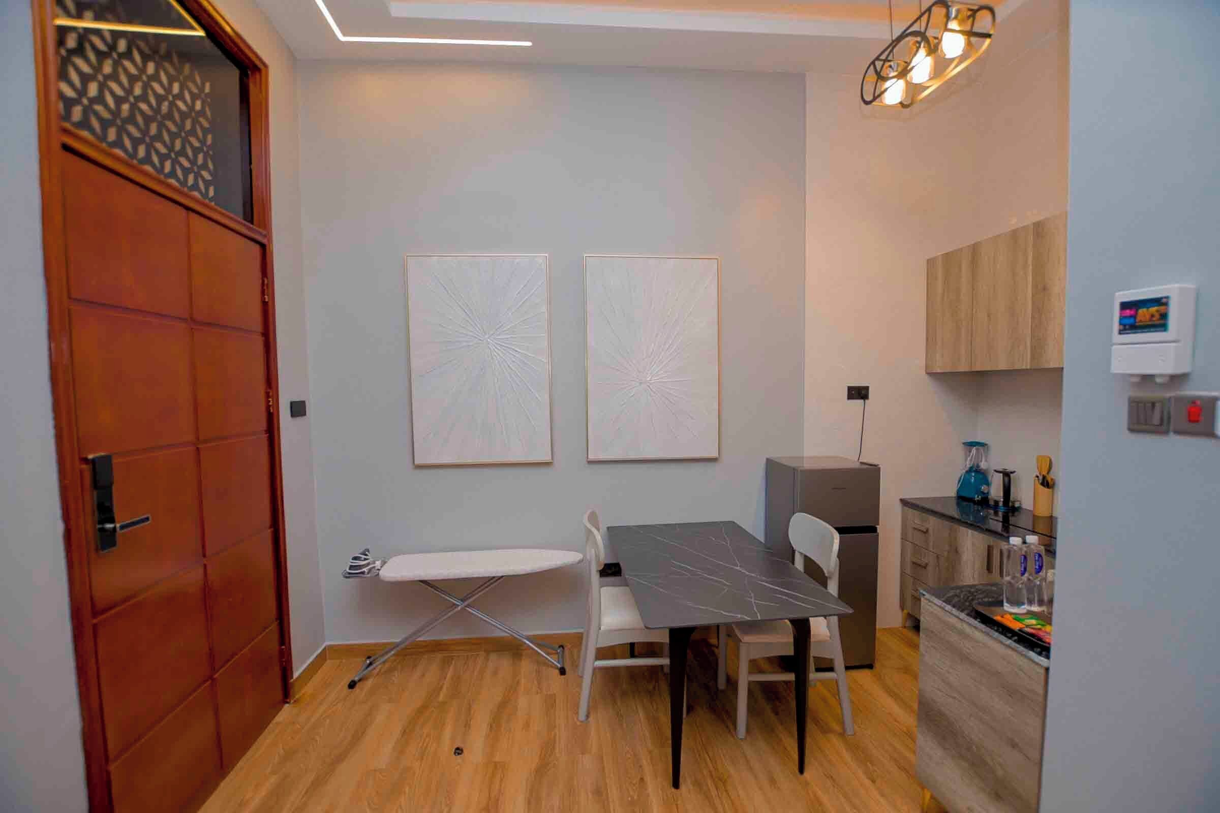 A compact kitchen with a dining area, a wooden door, and two wall-mounted artworks.