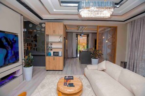 Ein modernes Wohnzimmer mit einem großen Flachbildfernseher, einem beigen Sofa, einem Holztisch und einer Kristallleuchter.