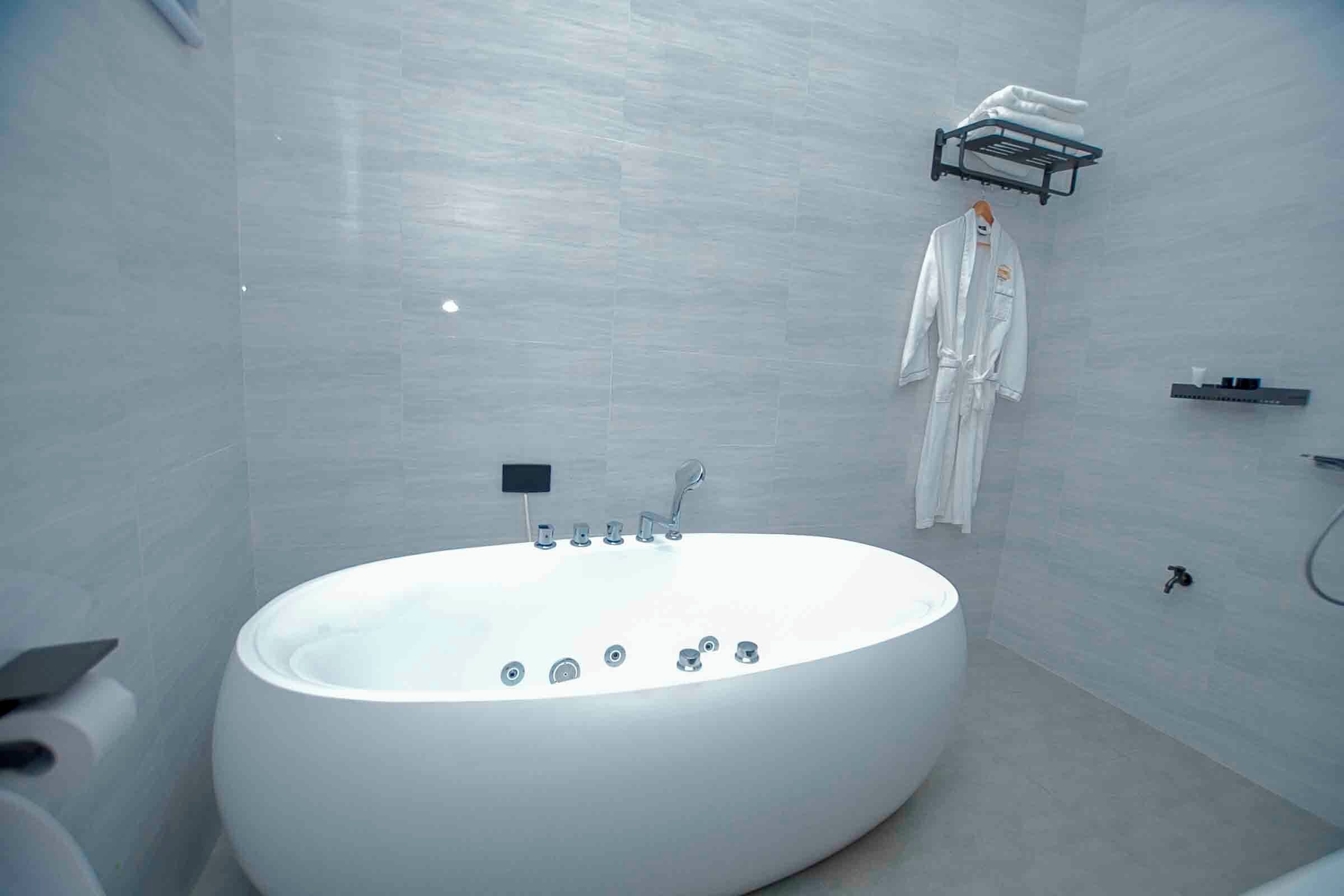 Un bagno moderno con una grande vasca ovale, un appendiabiti con un accappatoio e un piccolo ripiano con articoli da toilette.