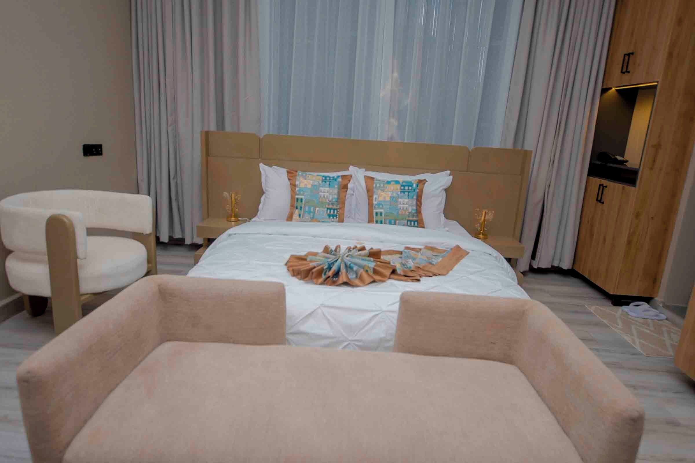 A hotel room with a large bed, a chair, a wooden cabinet, and a curtain.