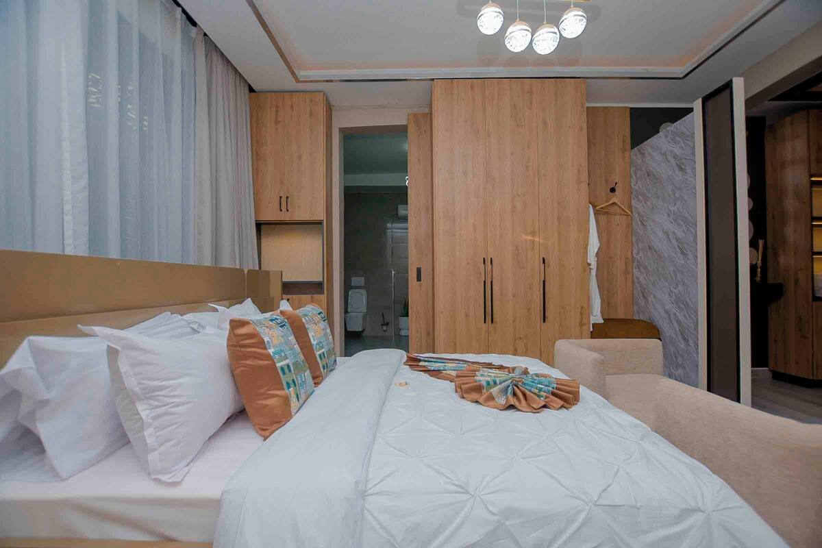 Una habitación de hotel moderna con una cama grande, un armario de madera y un baño visible a través de una puerta abierta.
