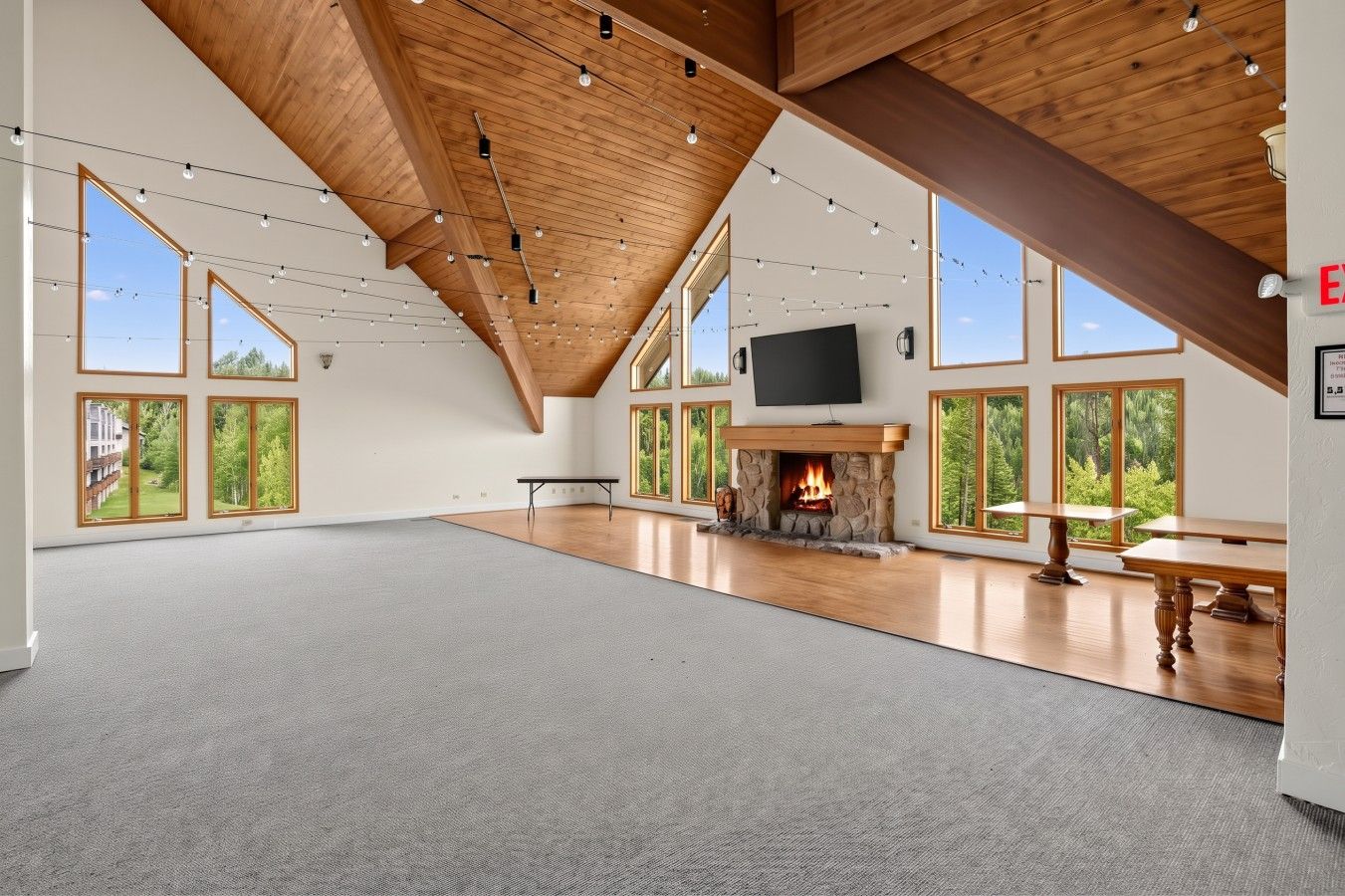 A spacious room with a high ceiling, large windows, a fireplace, and a flat-screen TV.