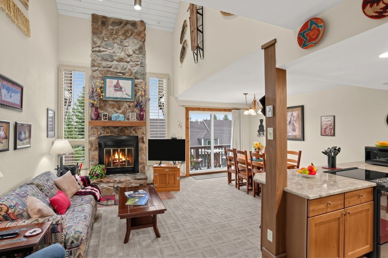 A spacious living area with a stone fireplace, a sofa, a coffee table, and a dining area with a kitchen island.