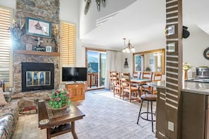 A spacious living room with a stone fireplace, a flat-screen TV, and a dining area with wooden chairs and a table. - Condo w Mountain Views, Jetted Tub and 2 Balconies (Durango)