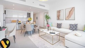 Une cuisine moderne avec des meubles blancs, un coin repas comprenant une table ronde et des chaises, un canapé blanc agrémenté de coussins à motifs, et deux tableaux abstraits accrochés au mur.