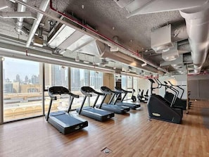 A modern gym with treadmills and exercise equipment, large windows offering city views, and exposed ductwork on the ceiling. - Vogue | Downtown with Direct Access to Dubai Mall (Dubai)