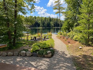 A lakeside deck with outdoor seating and a view of a lake surrounded by trees. - Hôtel à la maison - Le Loma-sur-le-lac avec spa! (Chertsey)