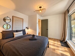 A bedroom with a bed, a bedside lamp, a ceiling fan, a window with curtains, and a door.