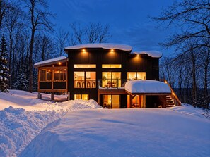 A multi-story cabin with a snow-covered roof, large windows, and a staircase leading to the upper levels. - Hôtel à la maison - Le Loma-sur-le-lac avec spa! (Chertsey)