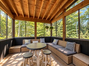 Un'area salotto esterna coperta, con tetto in legno, ampie finestre e mobili in vimini.