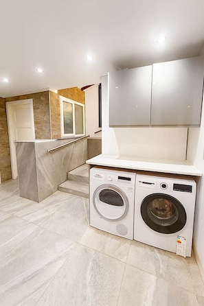 Un espace buanderie comprenant un lave-linge et un sèche-linge, une petite marche menant à une porte, et un mur en pierre.