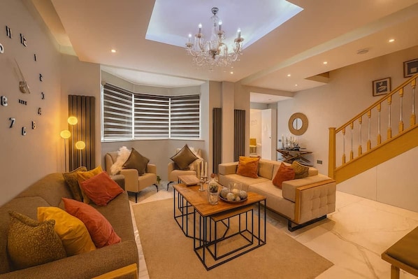 A modern living room with a sofa, armchairs, a coffee table, and a staircase.