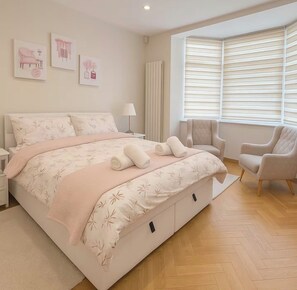 Une chambre avec un grand lit, deux chaises, un radiateur et des œuvres d’art accrochées au mur.