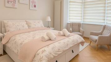 A bedroom with a large bed, two chairs, a radiator, and artwork on the wall.