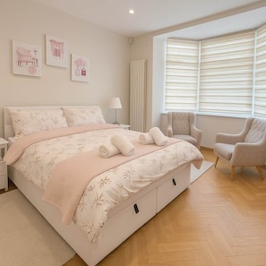 A bedroom with a large bed, two chairs, a radiator, and artwork on the wall.