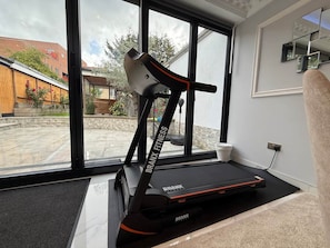 Een huisgymnasium met een loopband, een hometrainer en een raam met uitzicht op het omliggende landschap.