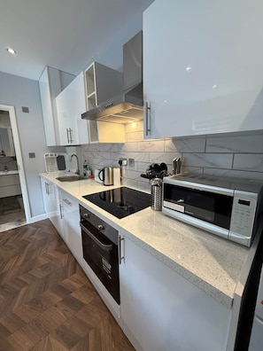 A modern kitchen with white cabinetry, a black induction cooktop, a built-in oven, and a microwave. - Beautiful Luxury home London | 10 bed 7 Bathroom (London)
